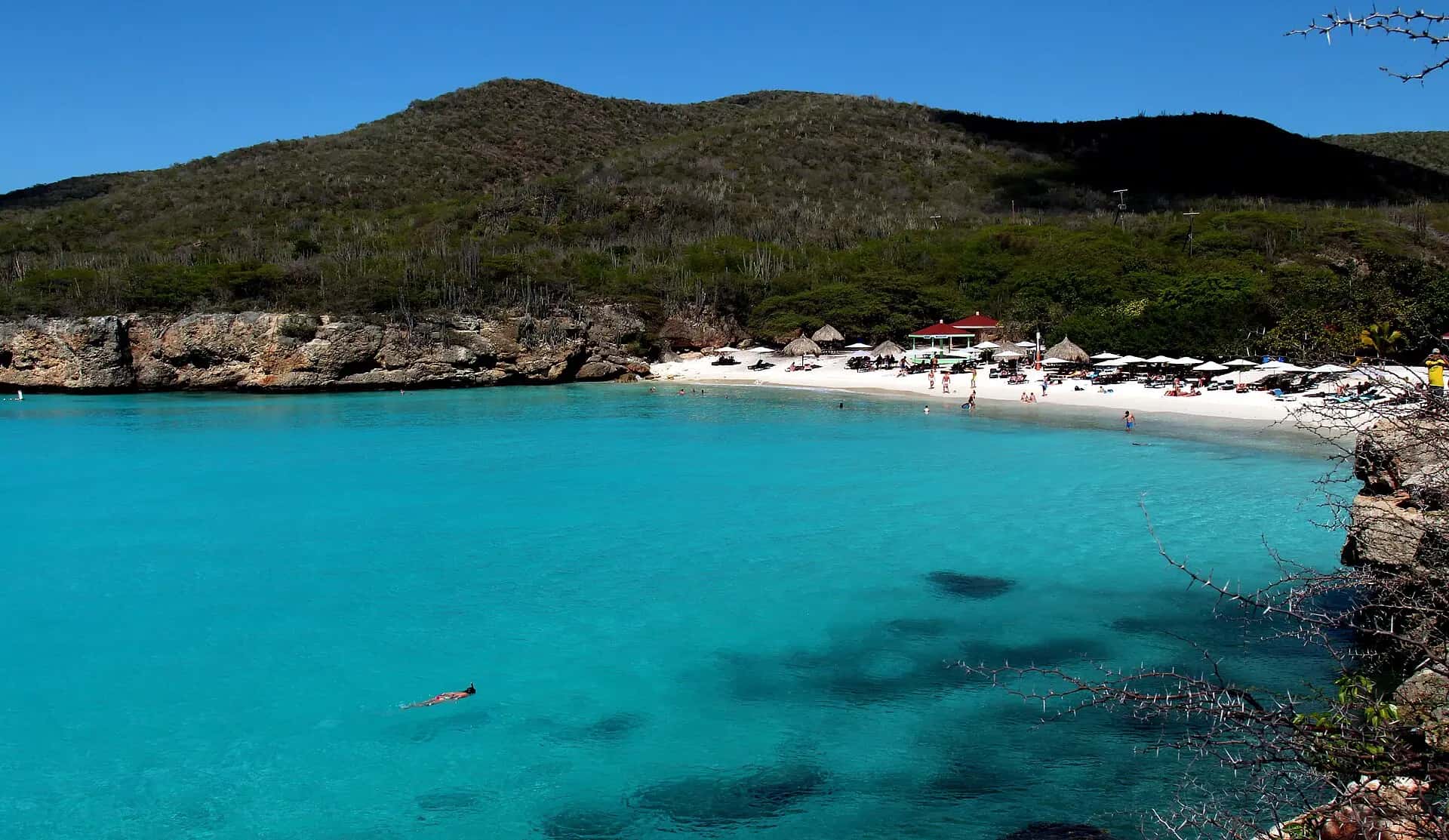 A turquoise cove below green hills at Playa Kenepa Grandi, Curaçao